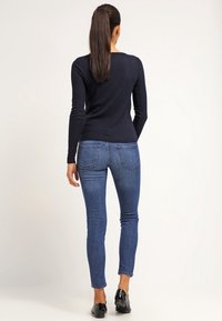 Haut à manches longues côtelé bleu marine associé à un jean bleu slim. La tenue présente une texture lisse et un design simple. Des chaussures noires complètent le look.