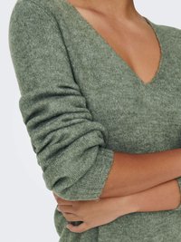 Maglione verde lavorato a maglia con scollo a V, caratterizzato da un tessuto texturizzato e maniche arrotolate. Il materiale sembra morbido e confortevole con una lucentezza sottile.