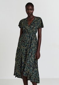 Robe portefeuille en tissu avec une base vert foncé et un motif de feuilles dorées. Présente des manches flottantes et une taille cintrée pour une silhouette fluide.