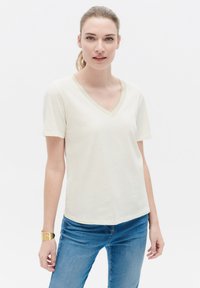 Kremowa koszulka z dekoltem w serek, uszyta z miękkiego materiału, z krótkimi rękawami i subtelnym, teksturowanym wykończeniem przy dekolcie. Standardowy krój.
