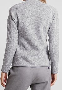 Grå fleece-pullover med texturerad yta, slim fit, hög krage och kontrasterande fåll. Har långa ärmar och mjukt material.