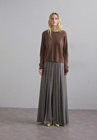 Brązowy sweter z dzianiny w wypukłe kropki, w połączeniu z długą szarym plisowanym spódnicą. Żółte buty dopełniają stylizację.