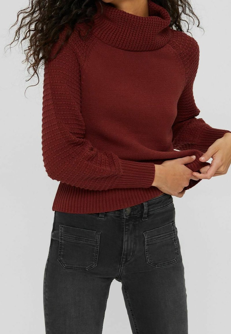 Pull en maille bordeaux avec un col roulé. Doté de manches texturées et de poignets côtelés. Associé à un jean foncé.