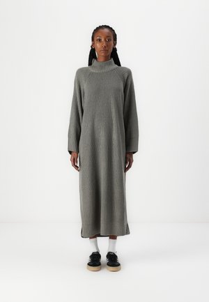 Gray knitted dress with a high collar, long sleeves, and ribbed texture, reaching mid-calf. Paired with black sneakers and white socks.