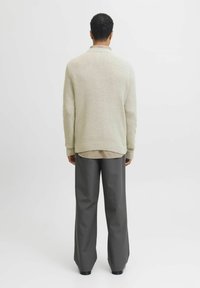 Gilet beige en tricot avec un motif texturé, col arrondi et poignets côtelés, associé à un large pantalon gris en tissu lisse.