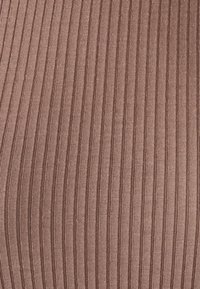 Tessuto a coste marrone con strisce verticali. La texture è morbida e presenta un aspetto leggermente elastico, evidenziando motivi sottili e uniformi.