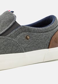 Slip-on sneakers with a gray textile upper, navy lining, brown leather accents, and white rubber sole. Features a decorative metal eyelet.