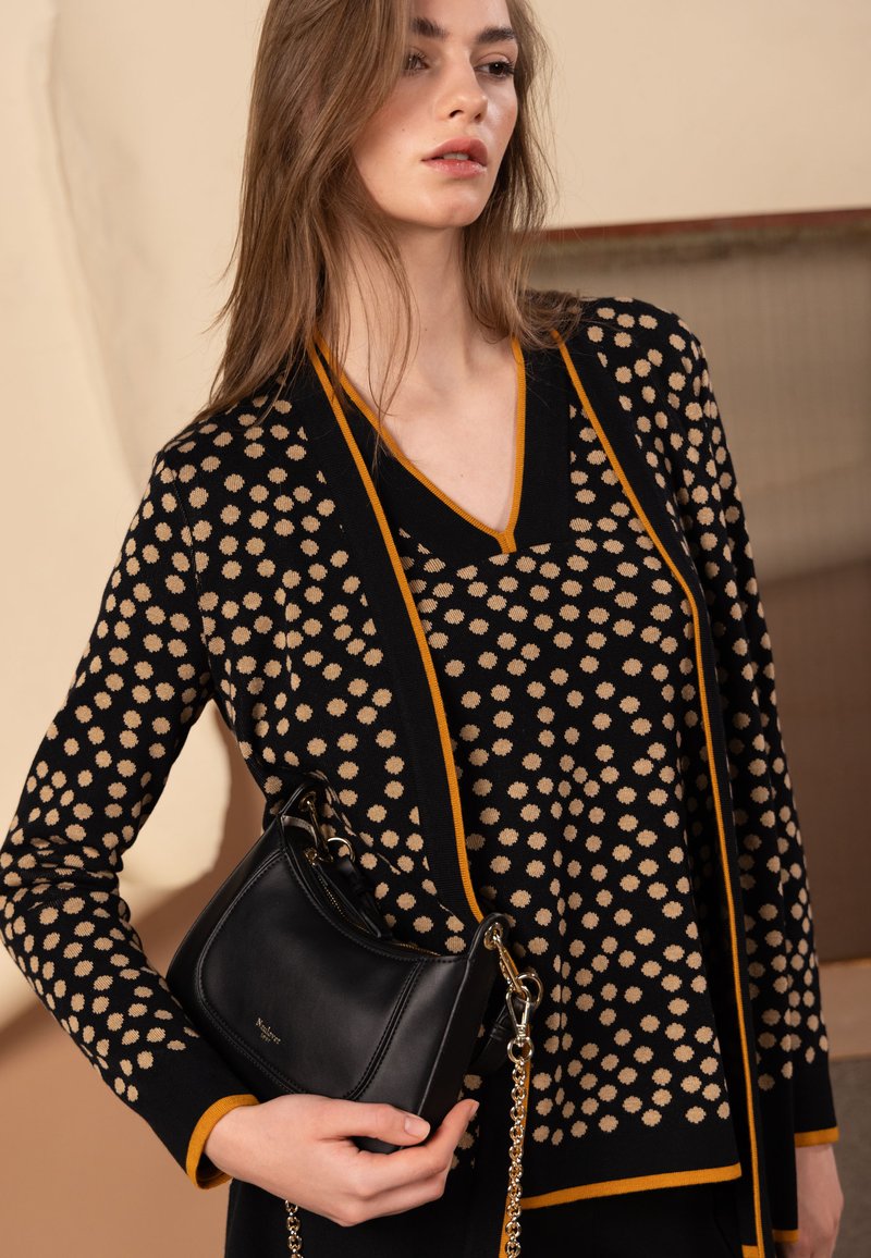 Svart och beige mönstrad stickad tröja med V-ringning och orange kant, kombinerad med en svart läderhandväska på en silverkedja.