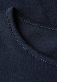 Nahaufnahme eines navyblauen T-Shirt-Ausschnitts mit sichtbaren Nähten und feiner gerippter Baumwollstofftextur.