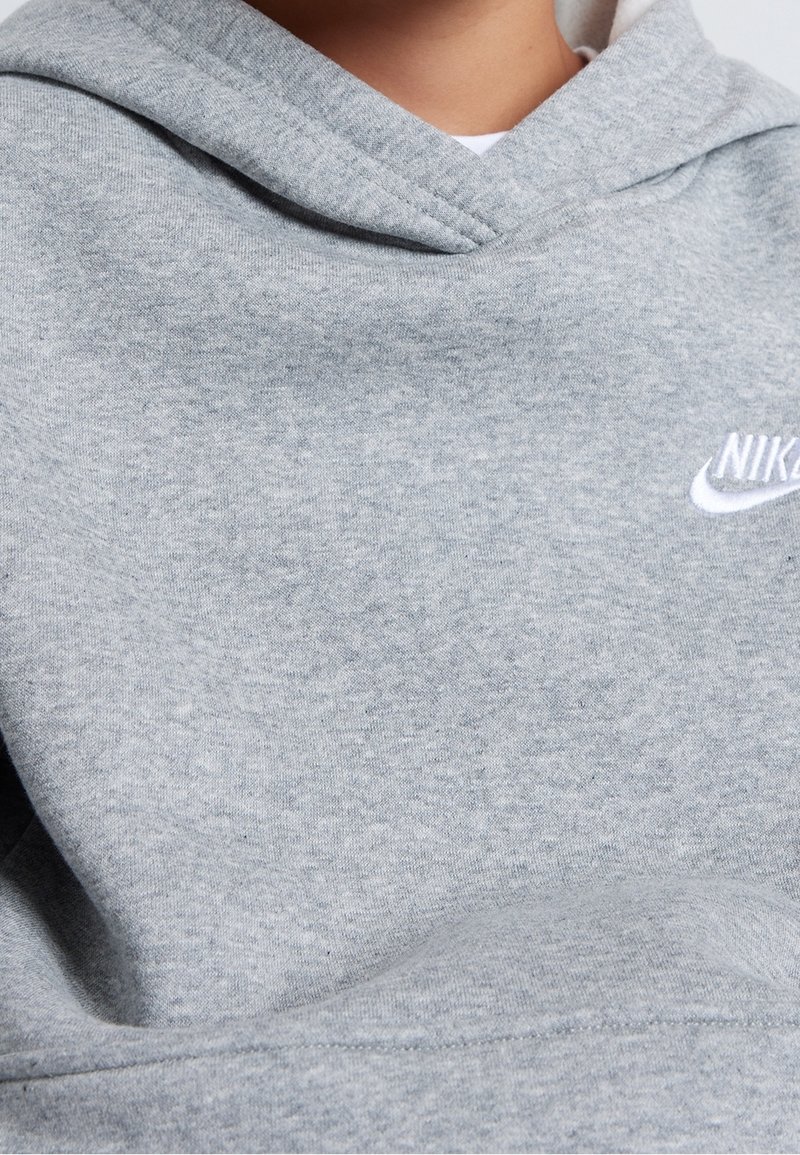 Grå hoodie tillverkad av mjuk bomullsblandningstyg, med en kenguruficka och en vit Nike-logotyp på bröstet. Texturerad yta synlig.