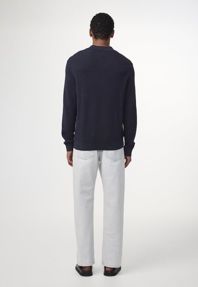 Marineblauer Strickpullover mit geripptem Muster, kombiniert mit hellgrauen Jeans. Das Outfit hat eine lockere Passform und dezente Details.