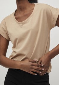 Beige bomullströja med rundad halsringning och uppvikta ärmar, med mjuk textur och avslappnad passform. Detaljerad handplacering vid midjan.