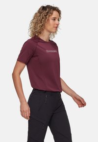 Vinröd kortärmad sporttröja med en logotyp, fastsydda sömmar och en jämn yta, i kombination med svarta cargobyxor med dragkedjefickor.