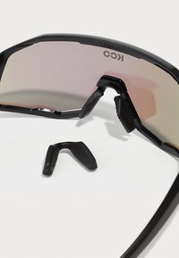 Black sports sunglasses with a curved lens, featuring a gradient tint and textured rubber nose pads. Includes a removable grip insert.