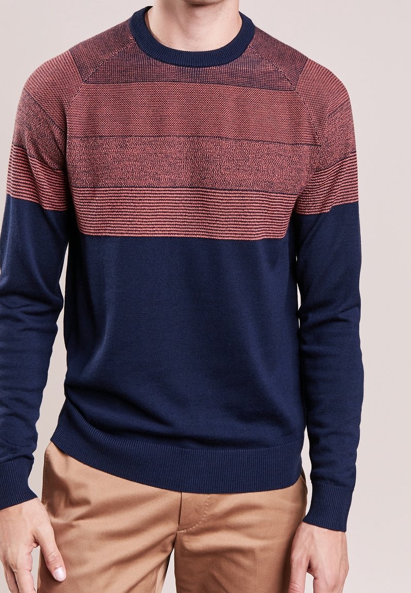 Dunkelblaues Sweatshirt mit einem strukturierten roten Streifenmuster über der Brust. Hat einen Rundhalsausschnitt sowie gerippte Bündchen und Saum. Glattes Strickmaterial.
