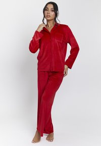 Rode fluwelen pyjama set met een knoopsluiting shirt met een zak en lange broek, beide van een gestructureerde stof en met een relaxte pasvorm.