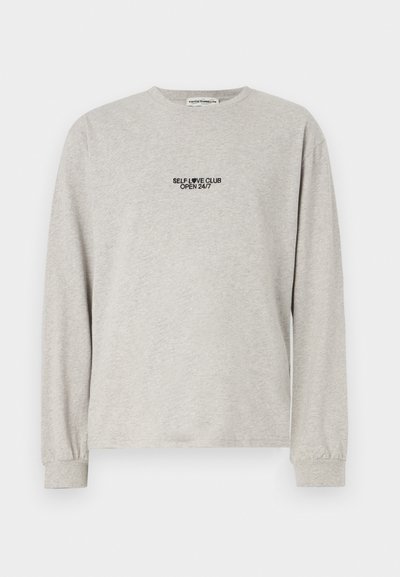 Gray long-sleeve t-shirt in soft cotton, featuring small black text on the front: "SELF LOVE CLUB OPEN 24/7." Simple crew neck and cuffs.