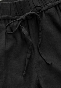 Los pantalones cortos de lino negro cuentan con una cintura elástica con un cordón de ajuste. La textura es suave, con pliegues sutiles en la cintura.