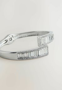 Silberne Armbanduhr mit rechteckigen Akzenten und klaren Steinen, mit einer glatten Oberfläche und einer sicheren Schließe. Sie misst ungefähr 6 mm in Breite.