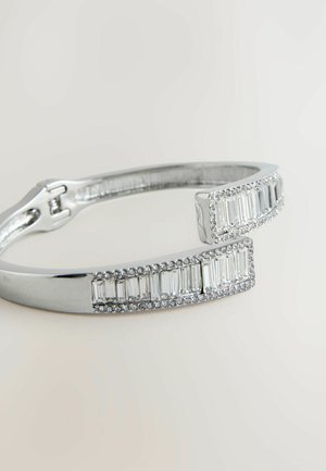 Hõbedane käevõru, millel on ristkülikukujulised aktsendid ja selged kivid, sile viimistlus ja turvaline haak. Laius umbes 6 mm.