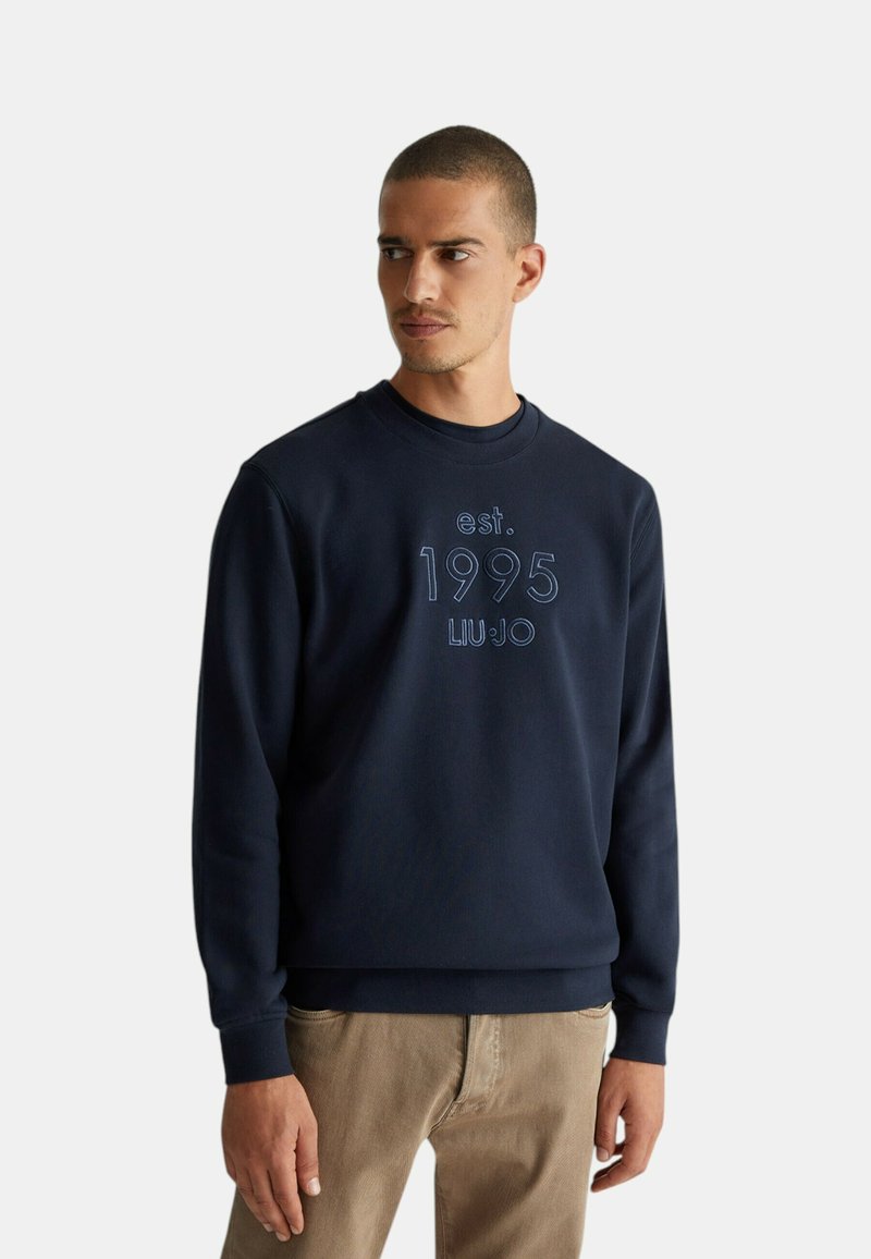 Felpa blu navy con la scritta "est. 1995 LIU JO" in rilievo sul davanti, colletto rotondo e polsini a coste. Texture morbida, vestibilità casual.