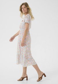 Blommig klänning med korta ärmar, elastisk midja och lageravskärning, med en vit bakgrund och flerfärgade små blommor. Bruna klacksandaler.