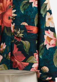 Σκούρο τιρκουάζ μπουφάν με μεγάλο ροζ, κόκκινο και λευκό λουλουδάτο σχέδιο, μπροστινή τσέπη με καπάκι και κουμπί και κέντημα "Barbour Farm Rio".