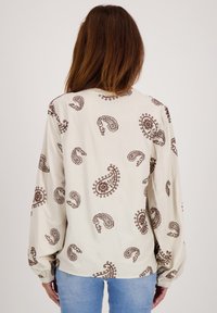 Langemouwen crèmekleurige blouse met een bruin paisleypatroon, zachte textuur en elastische manchetten. Ontworpen met een ronde halslijn en een ontspannen pasvorm.