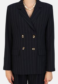 Blazer croisé à double boutonnage en tissu texturé à rayures bleu marine, avec des boutons dorés et deux poches avant.