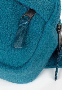 Tealkleurige fleece rugzakhoek met een gladde, afgeronde vorm. Voorzien van een nylon ritssluiting en een gestructureerd, zacht stoffen oppervlak.