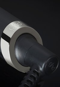 Close-up van een zwart haarstijl snoer dat is ingeplugd in een zilveren ring met "ghd" in beide delen gegraveerd.