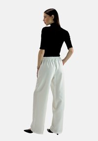 Top aderente nero con maniche corte abbinato a pantaloni bianchi a gamba larga con cintura elastica. Modella di spalle, indossa scarpe nere.