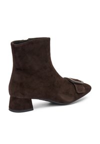 Bota de tobillo de ante marrón con punta afilada, un tacón de bloque y un detalle decorativo de hebilla en el costado. Textura suave y diseño elegante.