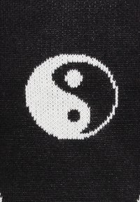Schwarzer Stoff mit einem weißen Yin-Yang-Symbol, das kontrastierende kreisförmige Formen hervorhebt, mit kleinen schwarz-weißen Punkten, die Dualität darstellen.