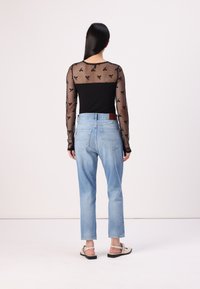 Top de malla negra de manga larga con patrón de mariposas, combinado con jeans rectos de color azul claro y calzado ligero. Diseño simple y moderno.