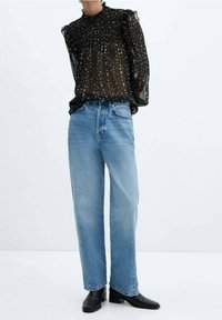 Sort transparent bluse med hvide polkaprikker og rynket hals, kombineret med lyseblå høj-taljede jeans og sorte ankelstøvler.