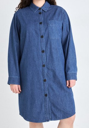 Robe-chemise en denim avec devant boutonné, manches longues, une poche poitrine unique et un ourlet incurvé dans une teinte bleu moyen.