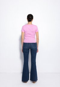 Dopasowana różowa koszulka w połączeniu z rozszerzającymi się ciemnoniebieskimi dżinsami, posiadającymi tylne kieszenie i teksturowaną tkaninę. Subtelne detale szwów.