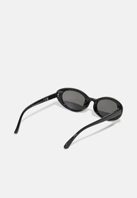 Black sunglasses with oval lenses, smooth plastic frame, gray tinted lenses, and slender temples. Features subtle branding on the inner arm.