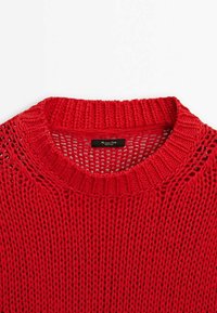 Pull rouge tricoté à col rond, présentant une maille ajourée et des poignets côtelés. Étiquette visible à l'intérieur près du col.