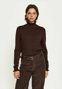 Pruun pikad varrukad turtleneck top, millel on tekstuuriga ribakanga ja volangkaelus. Kombineeritud pruuni kookospähkli pükste ja sobiva vöödiga.