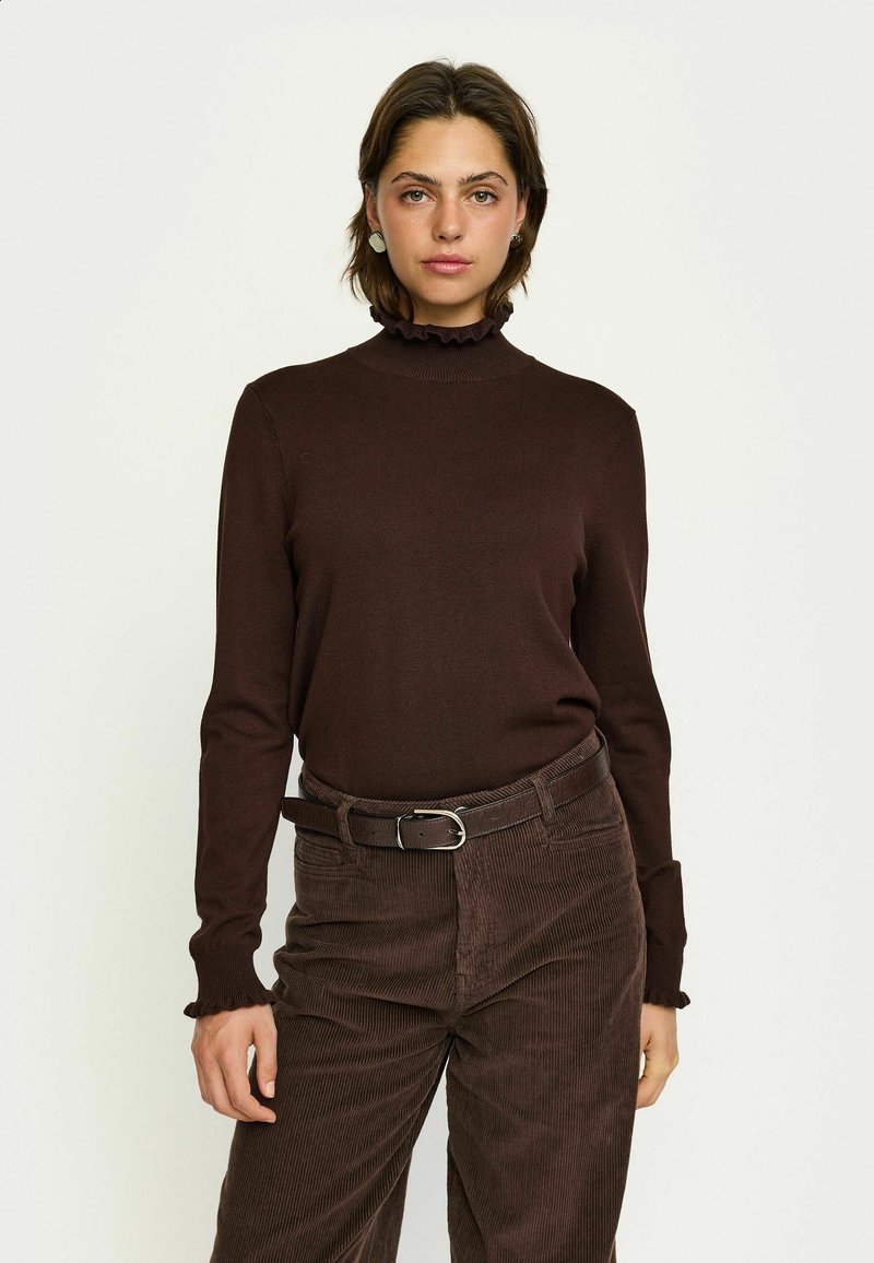 Pruun pikad varrukad turtleneck top, millel on tekstuuriga ribakanga ja volangkaelus. Kombineeritud pruuni kookospähkli pükste ja sobiva vöödiga.