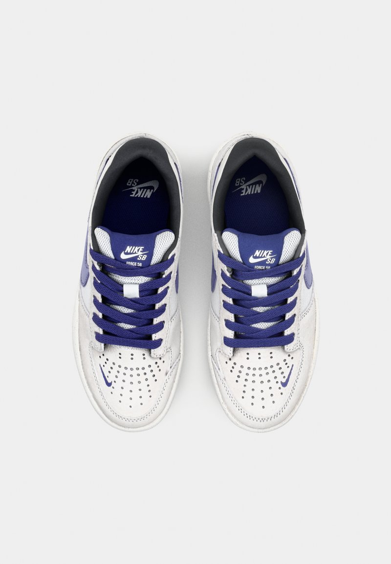 Weiße Nike SB Sneakers mit lila Akzenten, perforierter Zehenbox, weißen Schnürsenkeln und einer gebrandeten Innensohle. Klassisches Low-Top-Design.