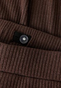 Pruun soonik Kangas, milles on õrn läige, must elastne pael ja ümmargune läbipaistev nööpiga detail.