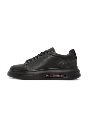 Zapatilla de cuero negro con punta redonda, parte frontal con cordones y amortiguación de aire en la suela. Presenta un panel lateral texturizado y detalles sutiles.