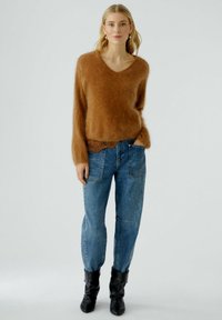 Brauner Mohair-Mix-Pullover mit V-Ausschnitt, kombiniert mit blauen, hoch taillierten Jeans aus Denim mit aufgesetzten Taschen und lockerer Passform. Schwarze Stiefeletten.