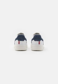 Białe sneakersy z granatowymi akcentami z zamszu, gumową podeszwą i małym czerwonym logo na pięcie, o gładkiej skórzanej konstrukcji.