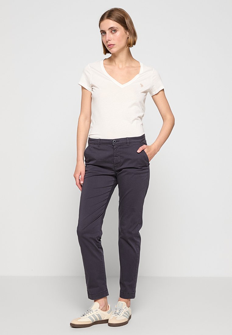 Casualny strój składający się z jasnobeżowej koszulki typu V-neck i ciemnonawowych spodni chino, uzupełniony jasnymi sneakersami z szarymi paskami i prostym logo.