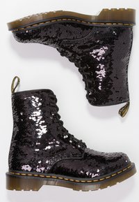 Botines negros con superficie de lentejuelas, punta redonda, diseño con cordones y suela de goma. Presentan costuras amarillas y una pestaña en el talón.