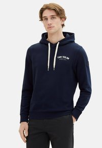 Felpa blu navy in cotone misto, con tasca frontale, cappuccio regolabile con lacci e logo bianco sul petto. Polsini e orlo a coste.